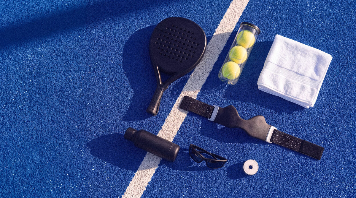 A court bag laid out on blue turf: racket, balls, towel, bottle, sunglasses and the strap