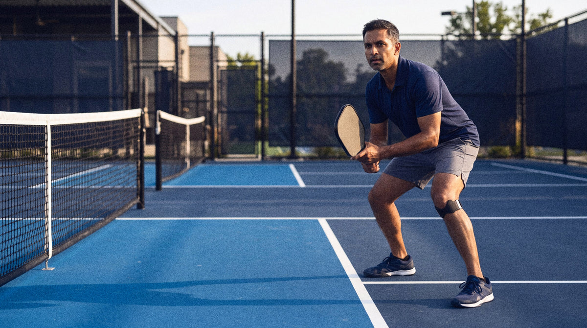 A pickleball player in a ready stance at the kitchen line wearing the strap