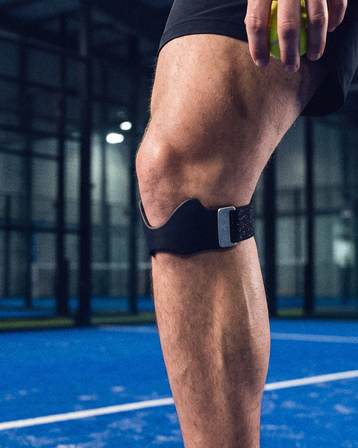 Close-up of the Second Set strap worn below the kneecap on an indoor padel court